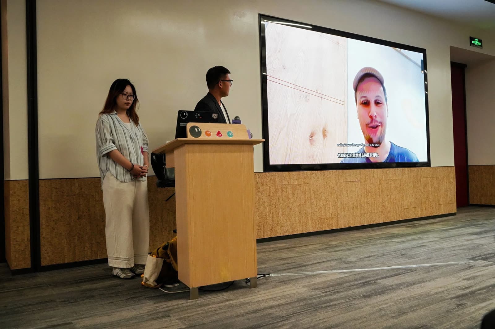 Grok Bot Meetup Beijing: hosts beside a video call on stage
